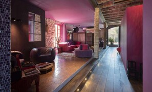 A modern interior with a stone wall, leather sofa, and a wooden floor. - Château & Village Castigno - Wine Hotel & Resort (Assignan)