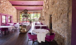 A restaurant with stone walls, round tables, and purple chairs. - Château & Village Castigno - Wine Hotel & Resort (Assignan)