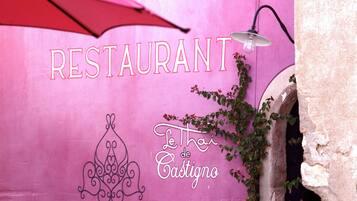 A pink wall with 'RESTAURANT' and 'Le Thai de Castigno' signage, a hanging light fixture, and a plant.