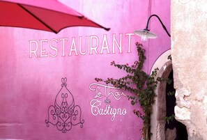 A pink wall with 'RESTAURANT' and 'Le Thai de Castigno' signage, a hanging light fixture, and a plant. - Château & Village Castigno - Wine Hotel & Resort (Assignan)