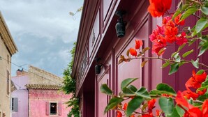 Una calle estrecha con un edificio de fachada rosa y un balcón con flores rojas.