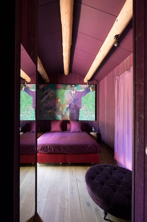 A bedroom with a wooden ceiling, a large abstract painting, a bed with red bedding, and a purple ottoman.. Château & Village Castigno - Wine Hotel & Resort