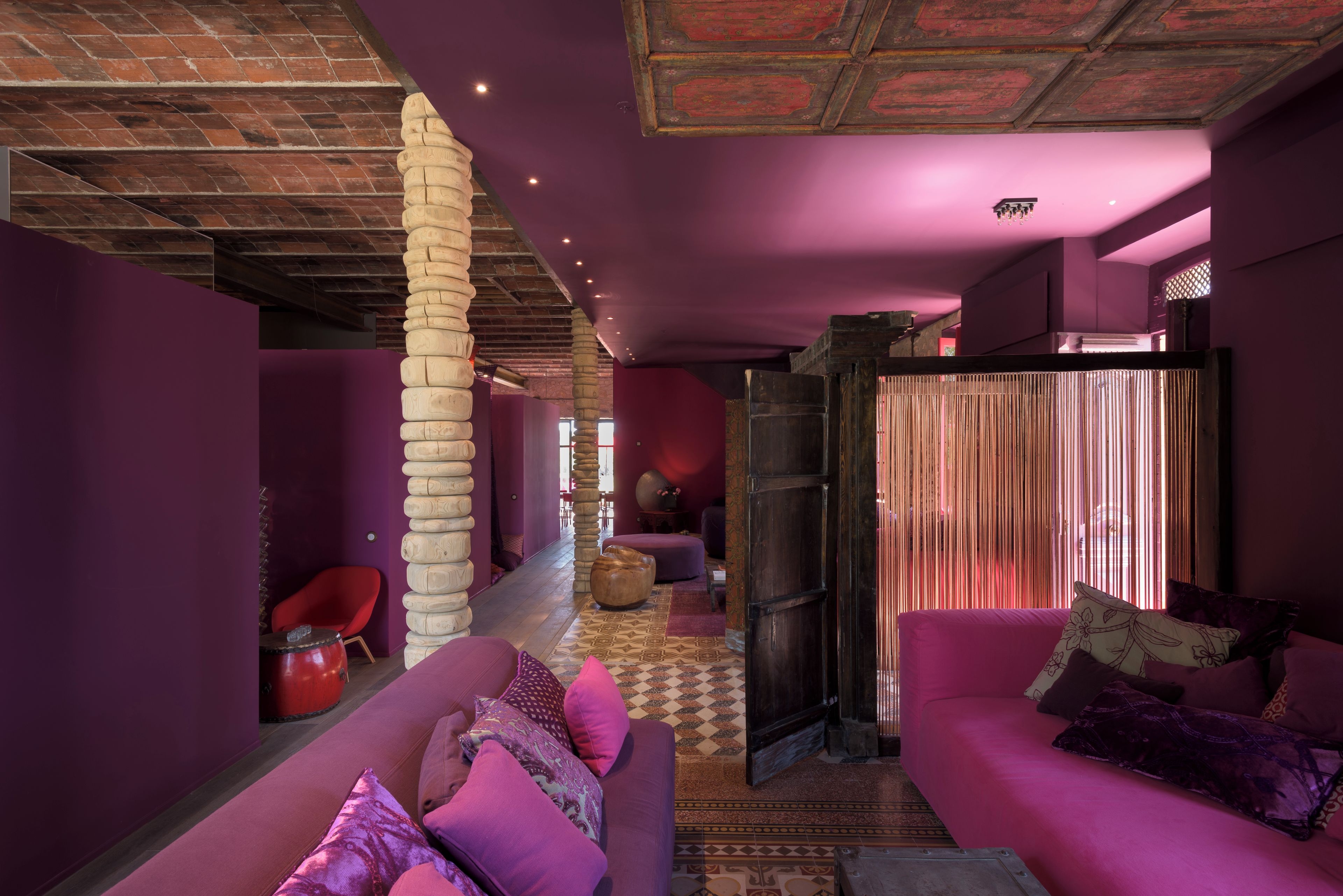 A modern interior with a purple color scheme, a stone pillar, a red chair, and a pink sofa.