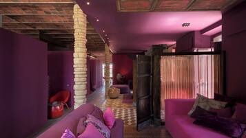 A modern interior with a purple color scheme, a stone pillar, a red chair, and a pink sofa.