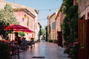 A cobblestone street with outdoor seating, buildings with shutters, and string lights. - Château & Village Castigno - Wine Hotel & Resort (Assignan)
