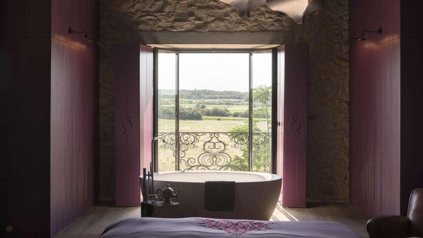 Un dormitorio con un ventanal grande, una bañera y vistas a un paisaje verde.