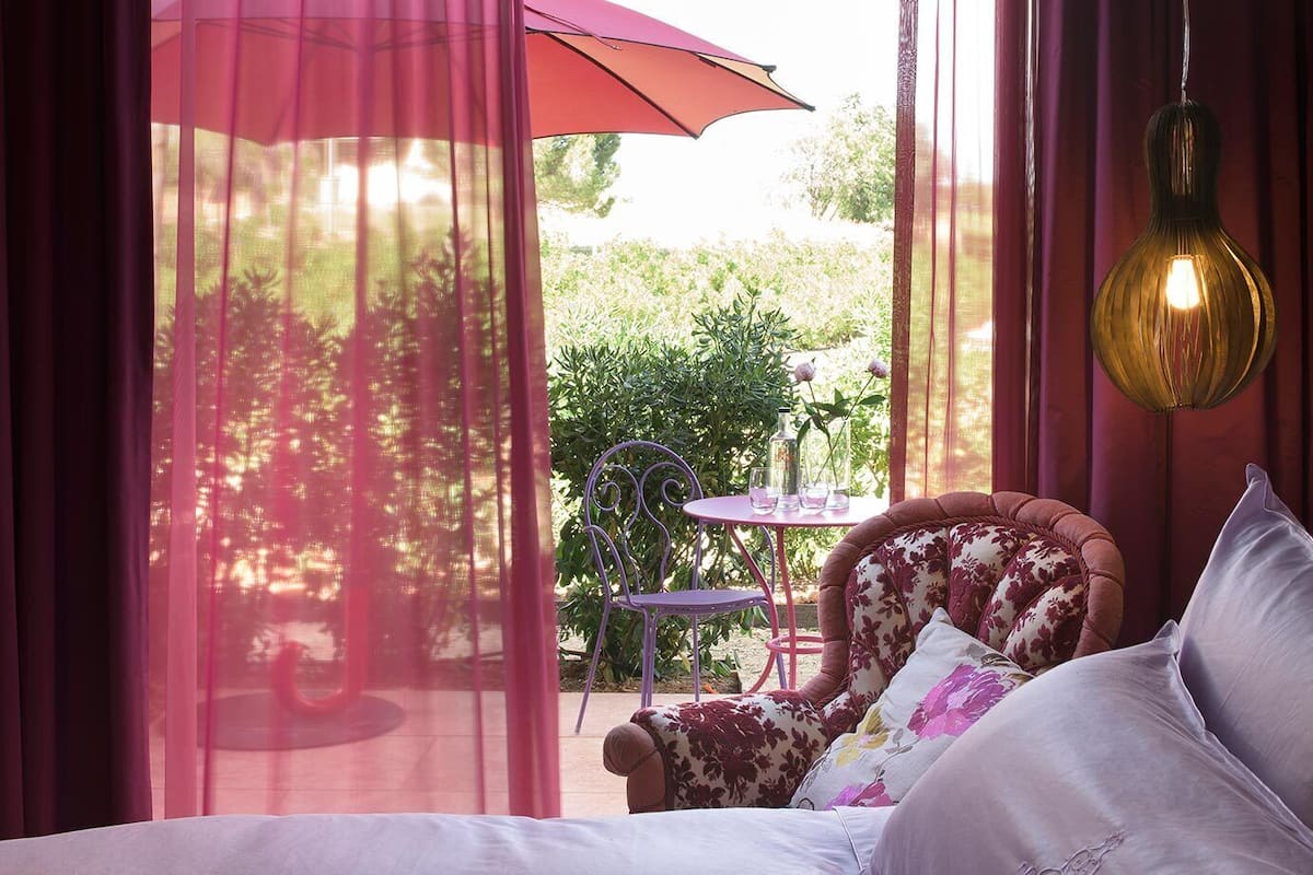 A bedroom with a bed, a chair, a table, and a hanging light fixture.