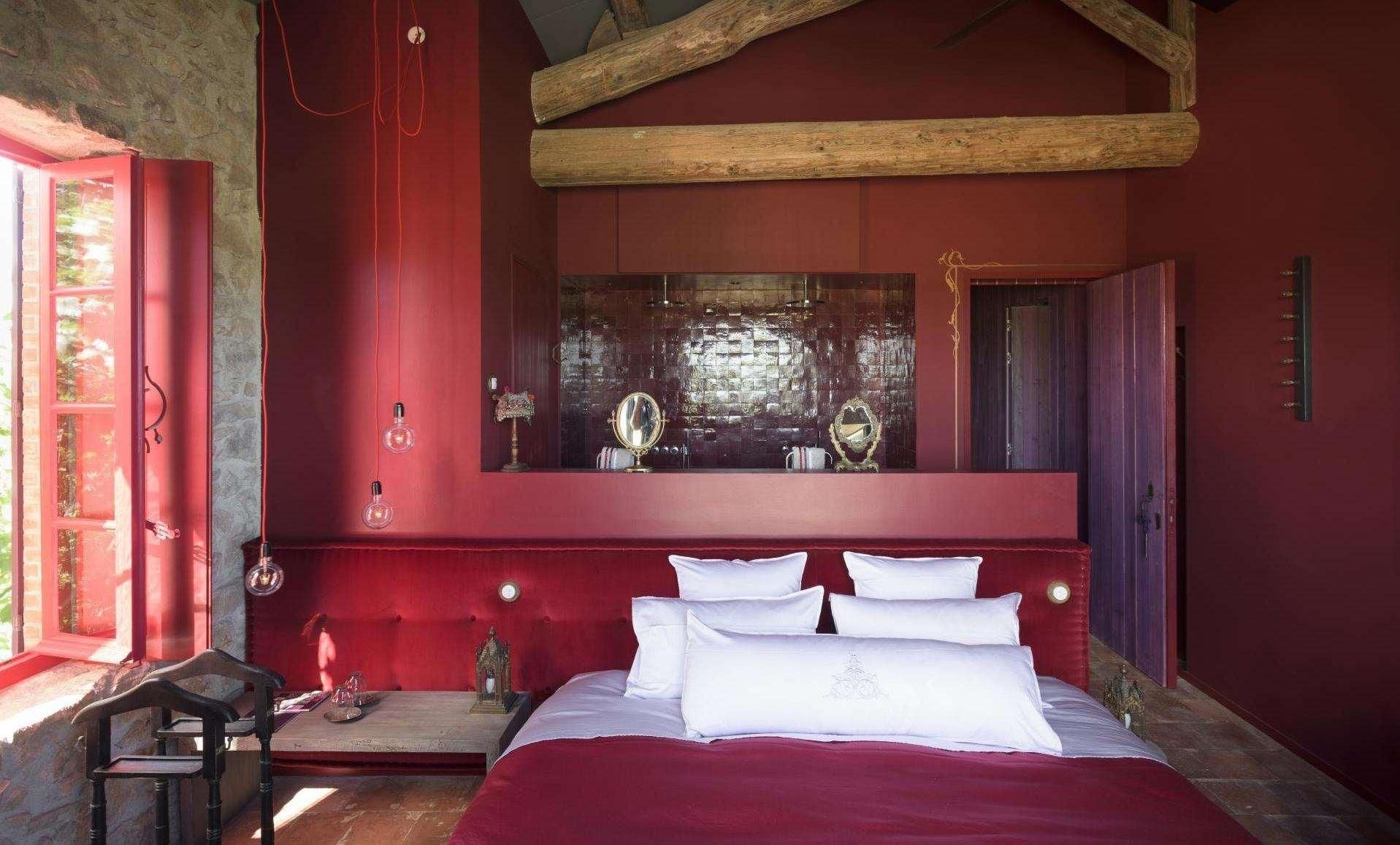 A red-walled bedroom with a large bed, a mirror, and a small table with a chair.