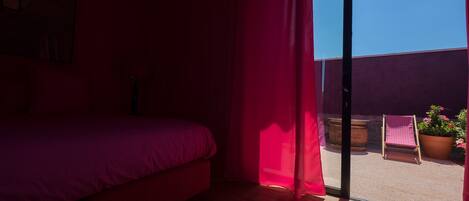 Habitación con cama, puerta corrediza de vidrio a un espacio exterior con una silla y plantas en macetas.