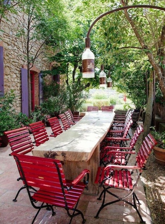 An outdoor dining area with a long table and red chairs, surrounded by stone walls and greenery.. Château & Village Castigno - Wine Hotel & Resort