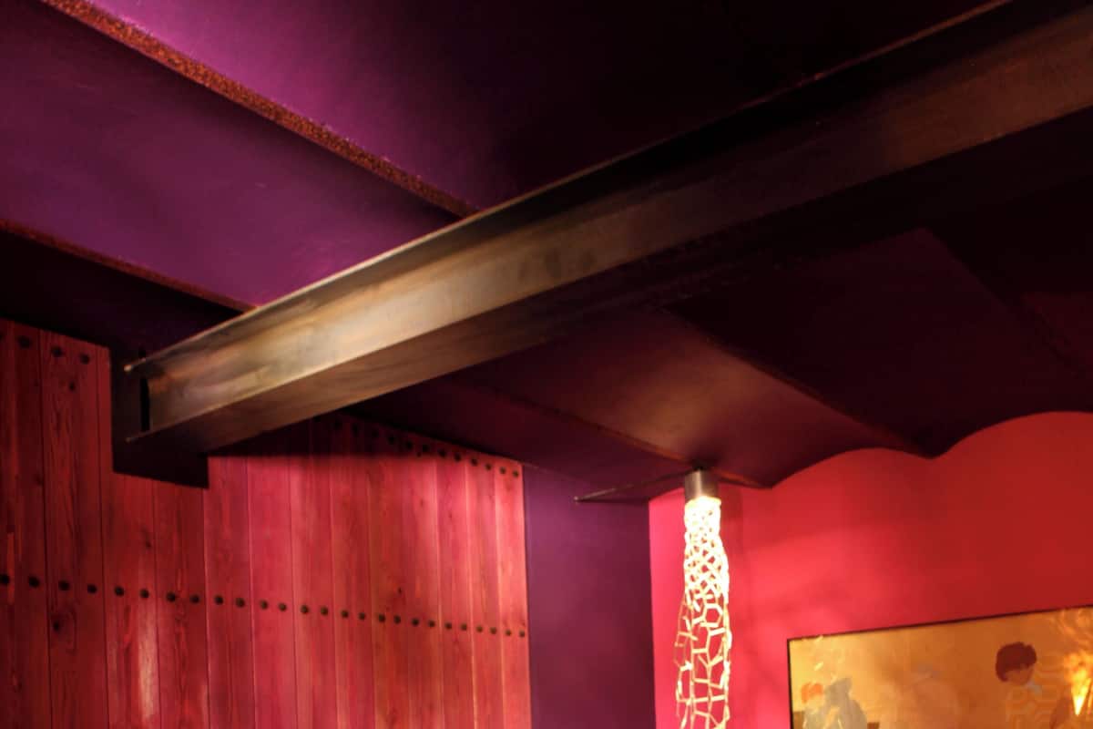 A bedroom with a bed, wooden headboard, a wall-mounted artwork, and a decorative light fixture.