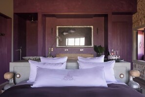 A bedroom with a large bed, a vanity with a mirror, and a stone wall. - Château & Village Castigno - Wine Hotel & Resort (Assignan)