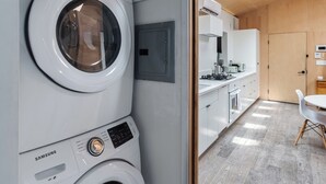 A laundry area with stacked washing machines and a view into a modern kitchen and dining area.