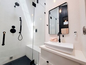 Ein modernes Badezimmer mit Duschkabine aus Glas, einem weißen Waschbecken und einem Spiegel mit schwarzem Rahmen.