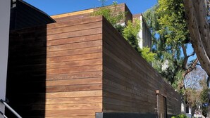 A modern building with a wooden facade, a black metal gate, and a sidewalk with a tree-lined path.