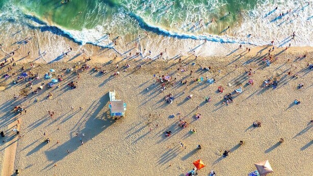 An aerial view of a beach with people, umbrellas, and a lifeguard stand.