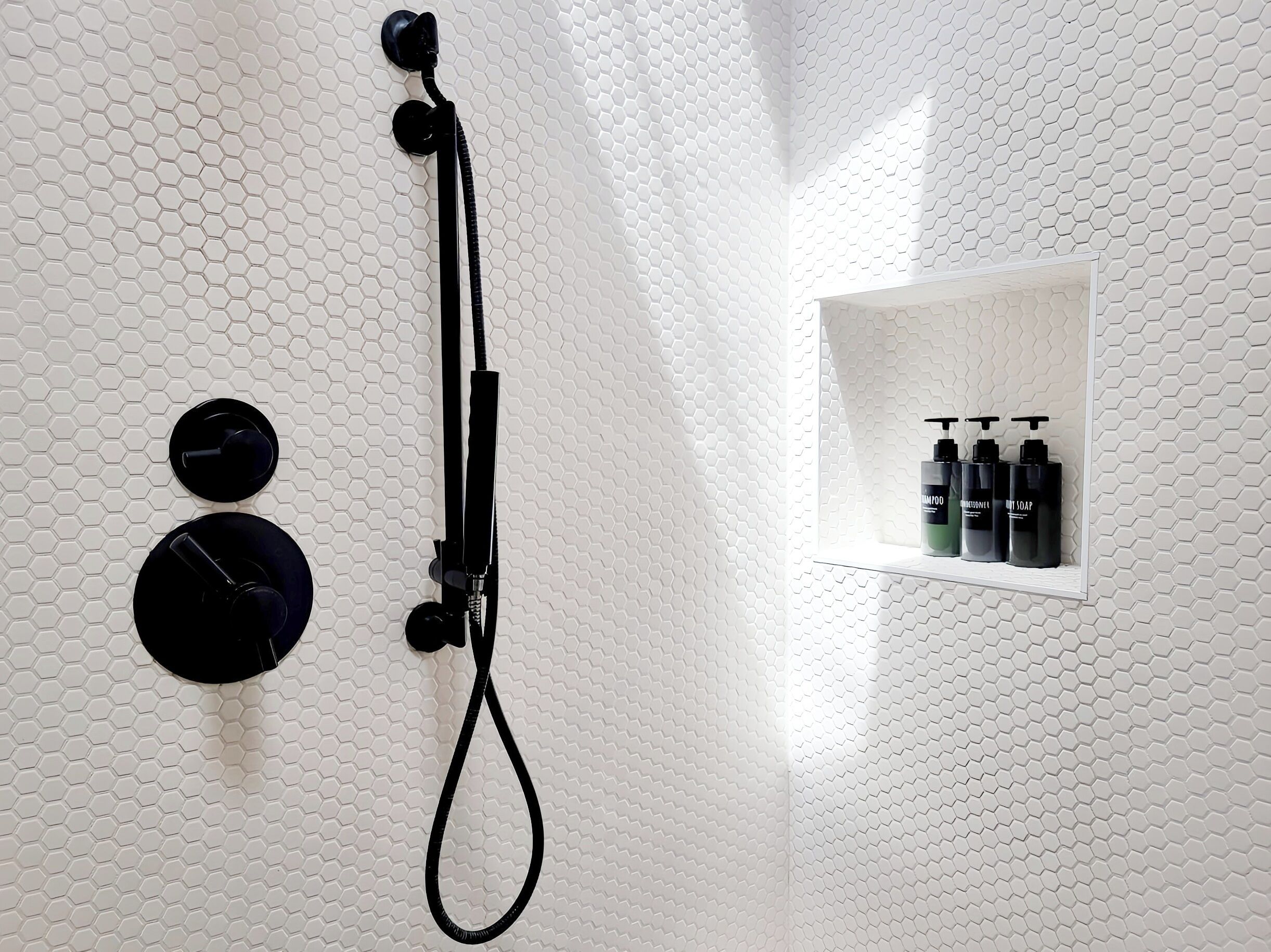 A bathroom with a shower, two round black fixtures, and a shelf with three black bottles.