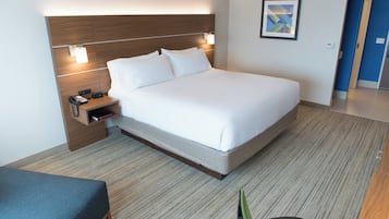 A hotel room with a large bed, bedside table with a phone, and a small reading area.