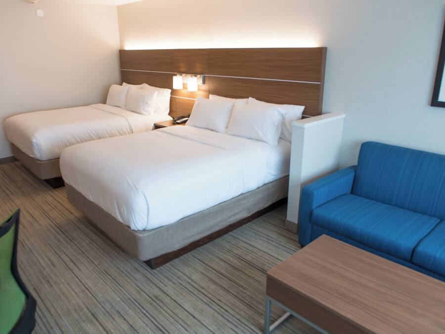 A hotel room with two beds, a blue sofa, a wooden nightstand, and a small table.