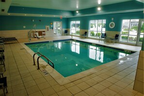 Una piscina interior con agua cristalina, suelo de baldosas y barandillas de seguridad.