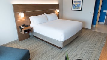 A hotel room with a large bed, bedside table with a phone and book, and a small desk with a chair.