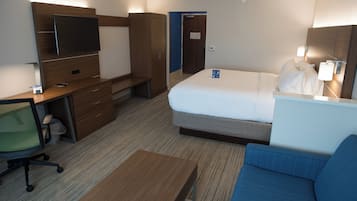 A hotel room with a bed, a desk, a chair, a TV, and a bedside table.