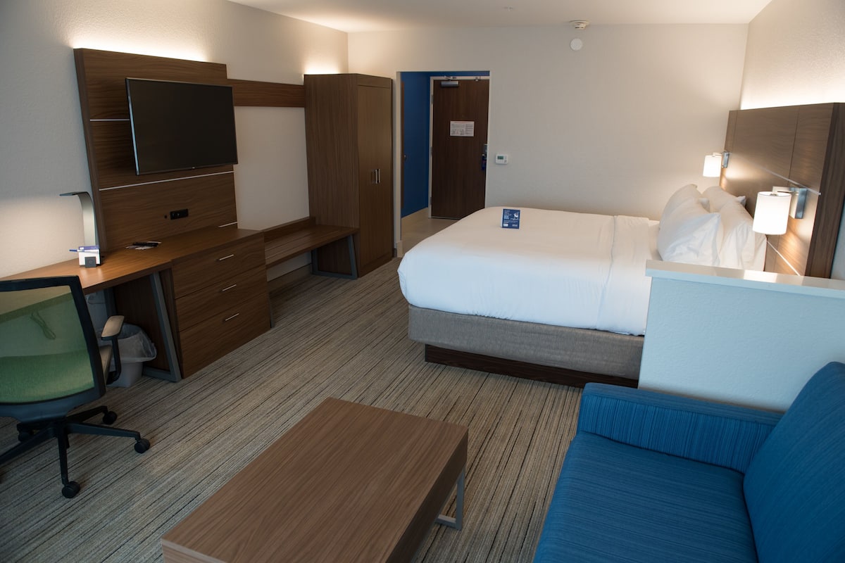 Et hotelværelse med en seng, et skrivebord med stol, et fjernsyn og en blå sofa.