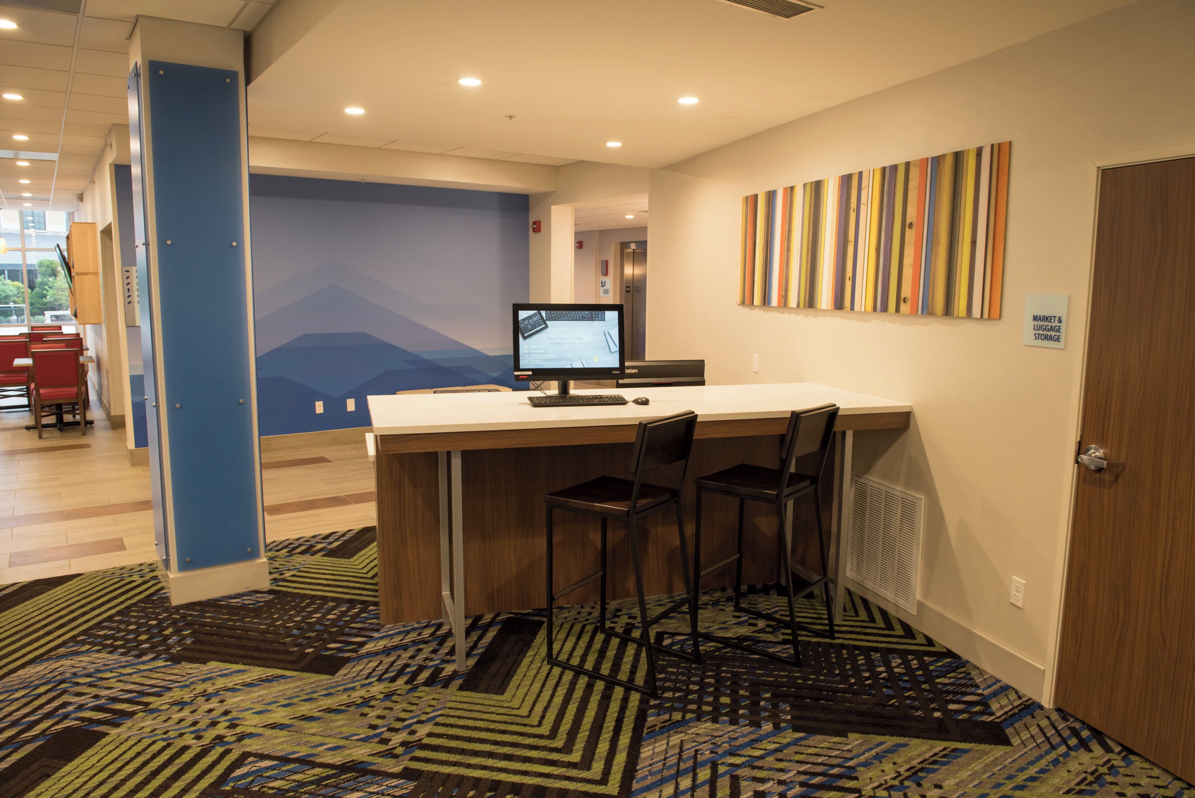 A hotel lobby with a reception desk, a computer monitor, and a seating area with chairs.