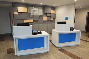 Two reception desks with digital payment terminals, a wall-mounted sign, and a security camera. - Holiday Inn Express & Suites Dayton North - Vandalia by IHG (Dayton)