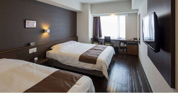 Une chambre d’hôtel avec deux lits, un bureau, une chaise, une télévision et une fenêtre avec des rideaux.