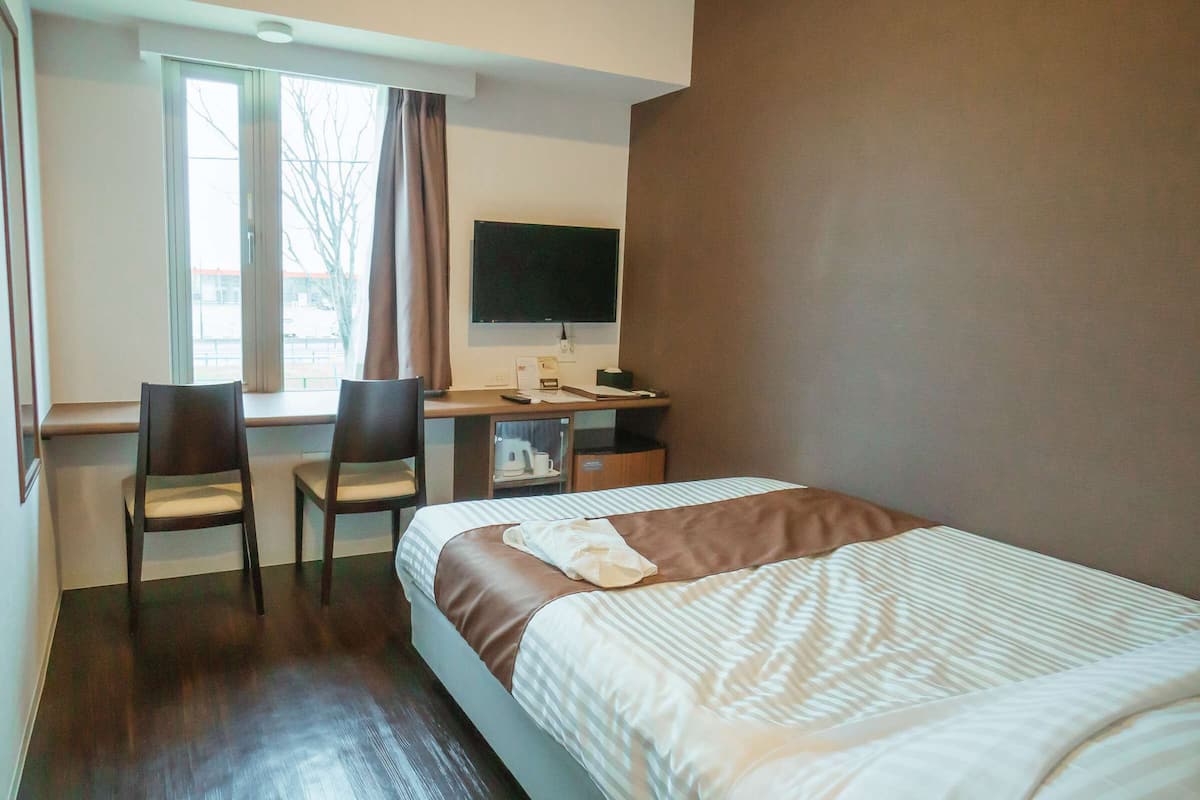 A hotel room with a bed, two chairs, a desk with a computer, and a window.