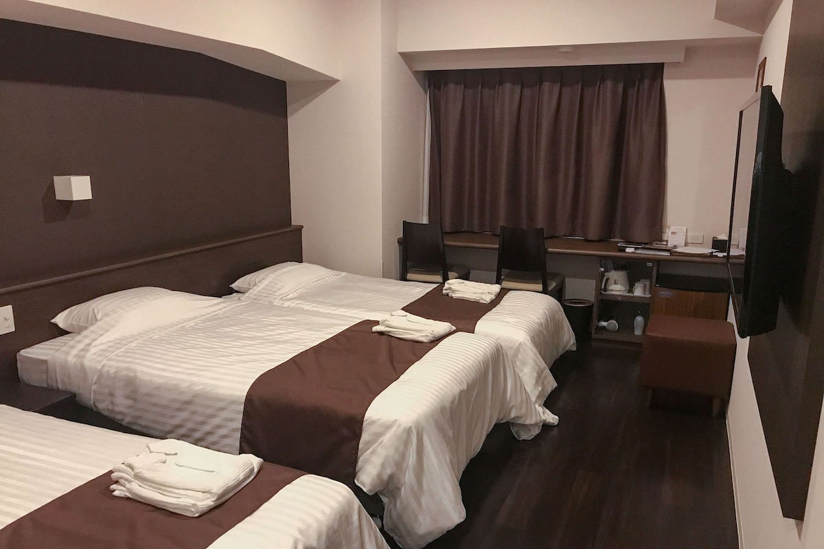 A hotel room with two beds, a desk, a chair, and a television.