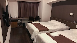 Une chambre d’hôtel avec deux lits, un bureau avec des chaises, une télévision et une fenêtre avec des rideaux.
