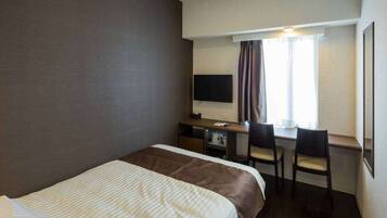 A hotel room with a bed, a desk with two chairs, a television, and a window with curtains.
