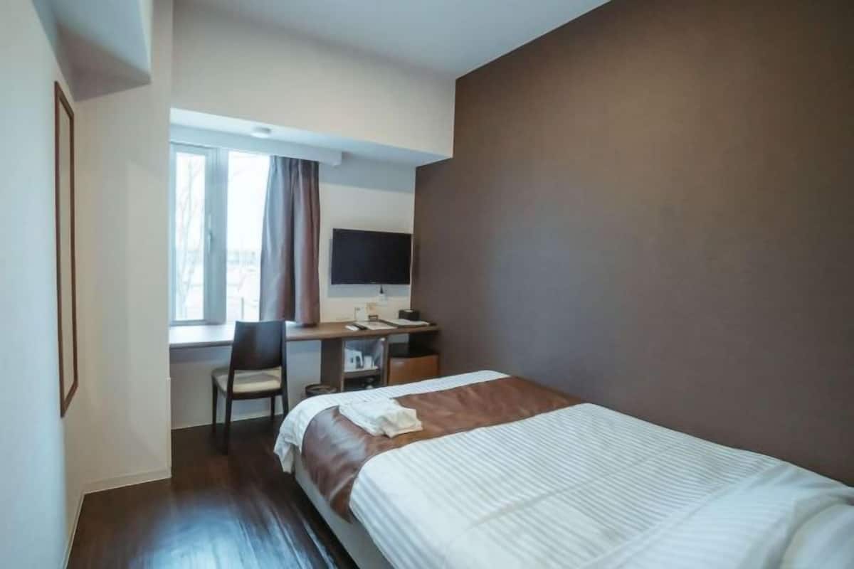 A hotel room with a bed, a desk, a chair, a television, and a window with curtains.