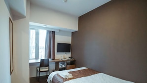 Une chambre d’hôtel comprenant un lit, un bureau avec un ordinateur et une chaise, une fenêtre avec des rideaux et un téléviseur à écran plat.