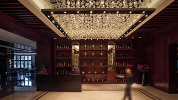 A lobby with a large chandelier, wooden shelving with decorative items, and a reception desk.