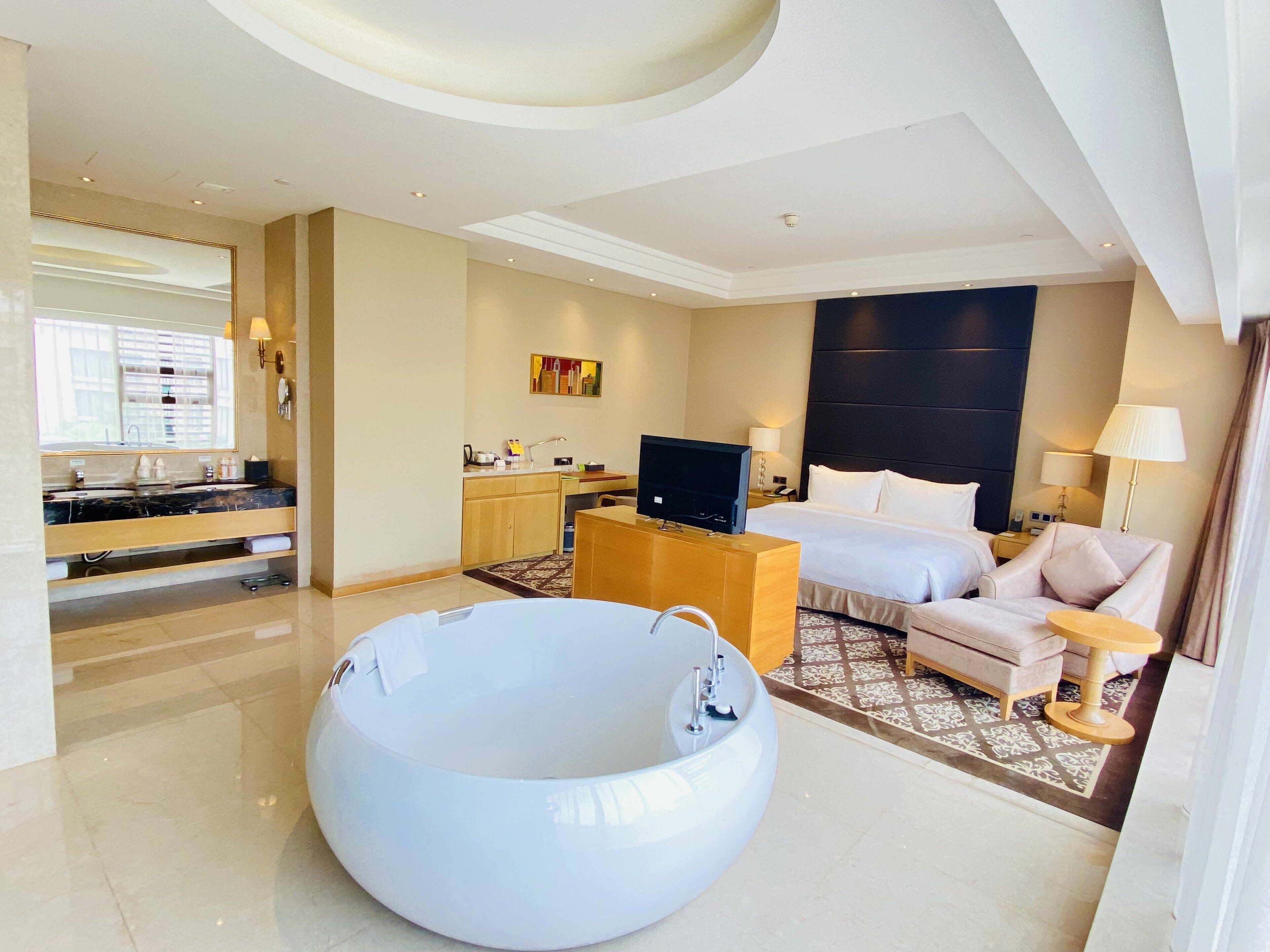 A hotel room with a large bathtub, a bed, a desk, and a television.