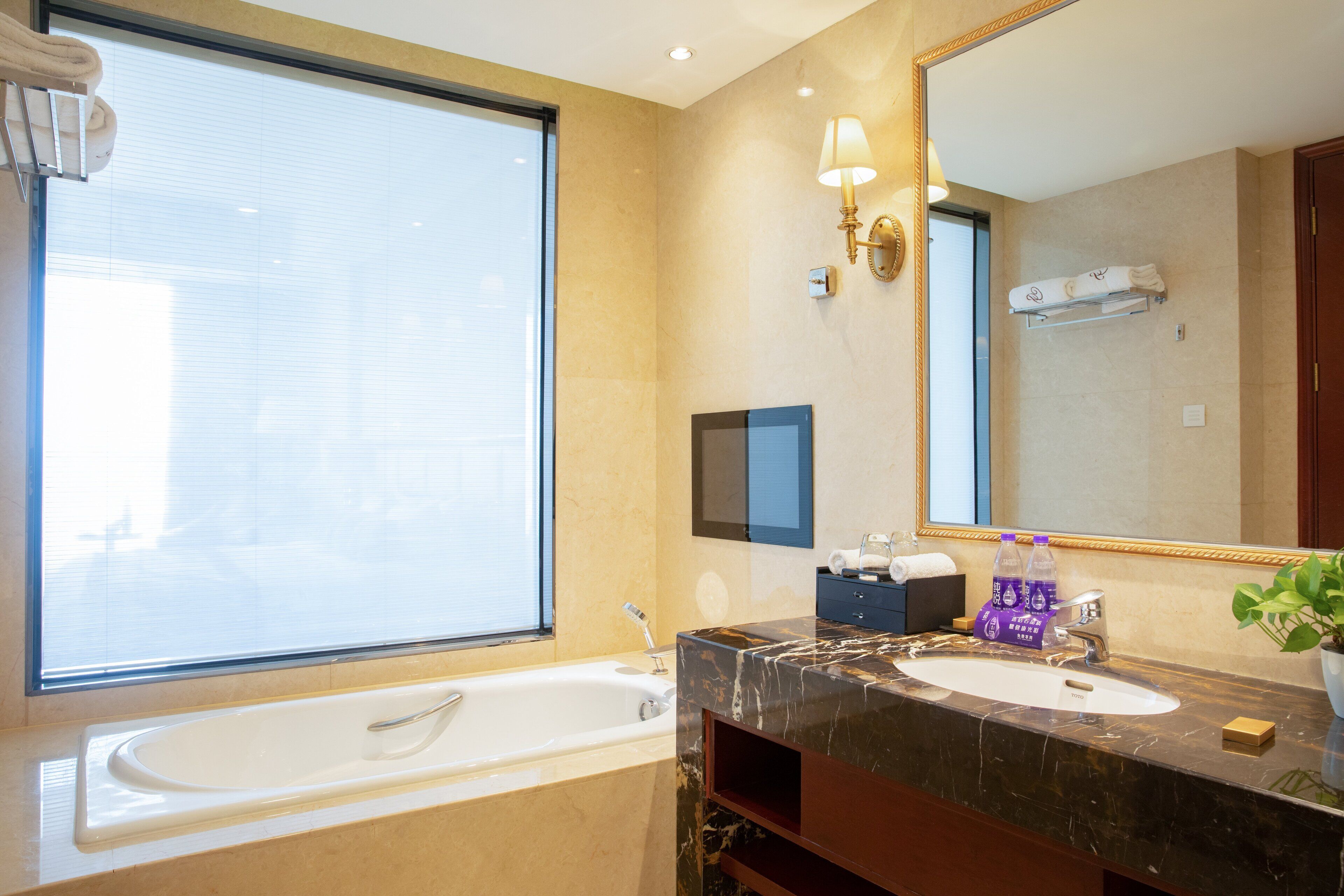 A modern bathroom with a large window, a bathtub, a vanity with a marble countertop, and a mirror.