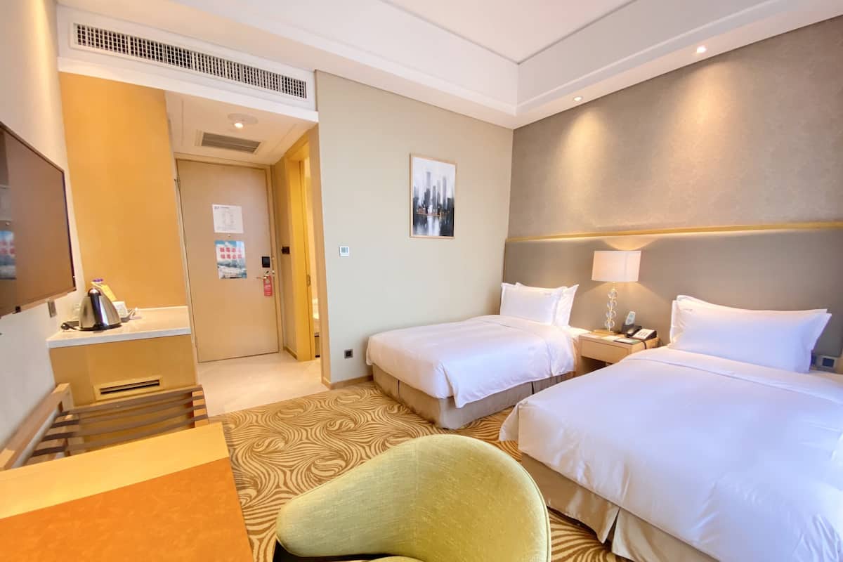 A hotel room with two beds, a desk with a chair, a TV, and a patterned carpet.