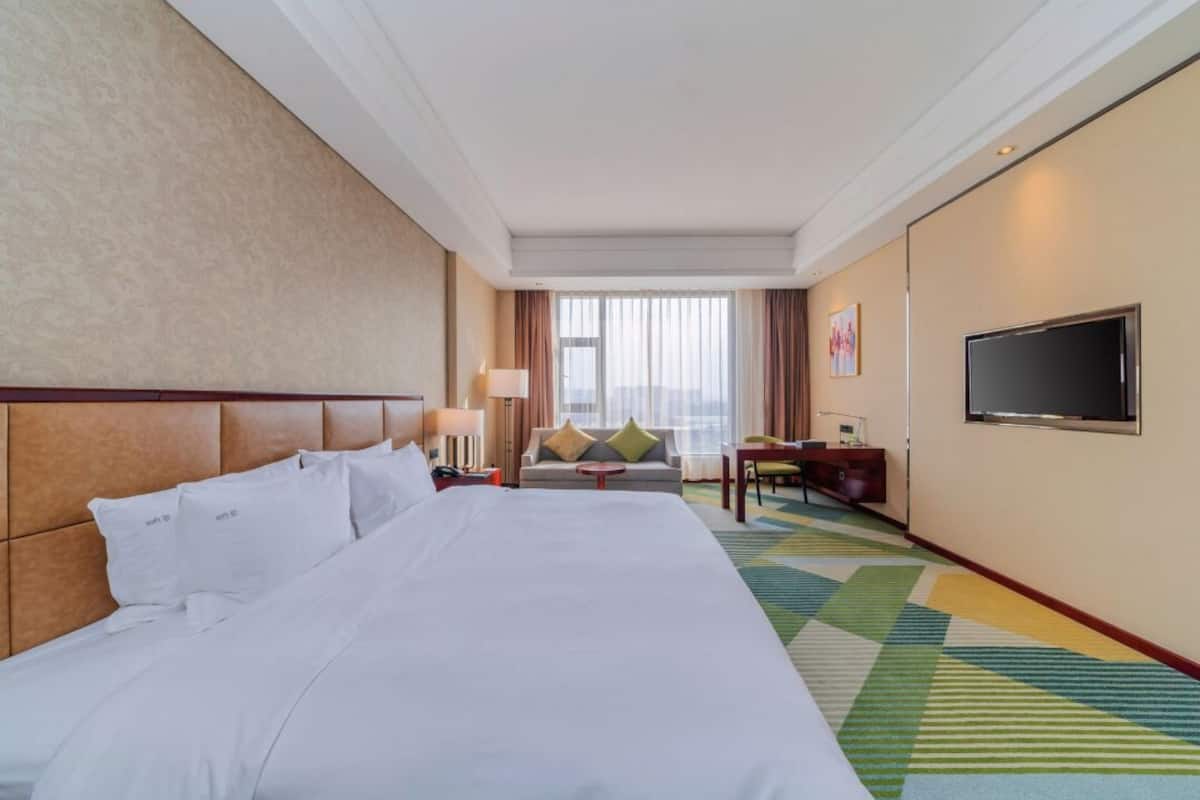 A hotel room with a large bed, a sofa, a TV, and a window with curtains.