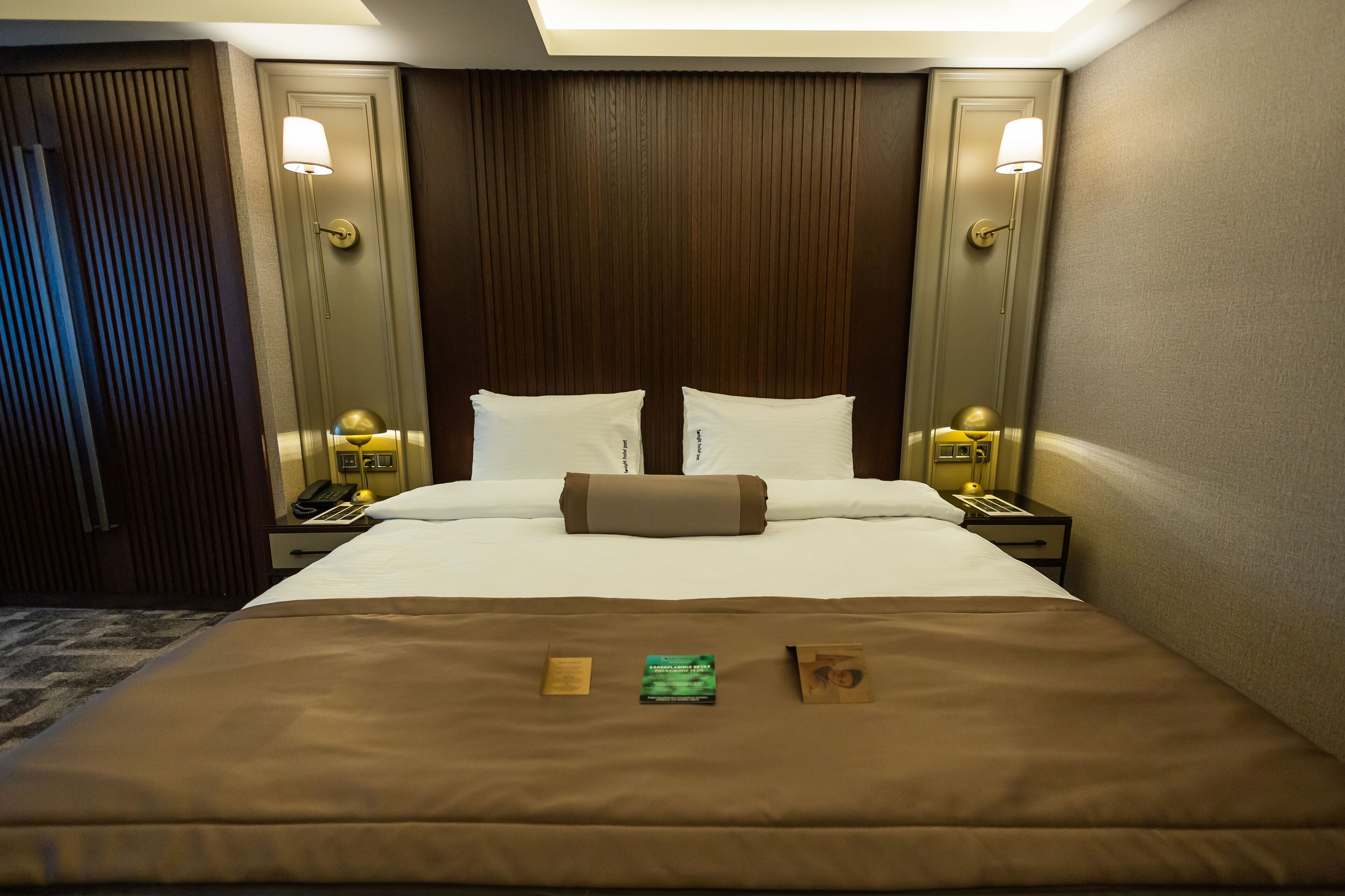 A hotel room with a large bed, two bedside tables with lamps, a wooden headboard, and a carpeted floor.