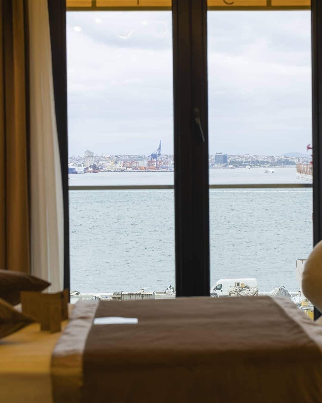 A hotel room with a large window offering a view of a city skyline and a body of water.