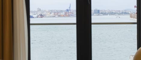 A hotel room with a large window offering a view of a city skyline and a body of water.