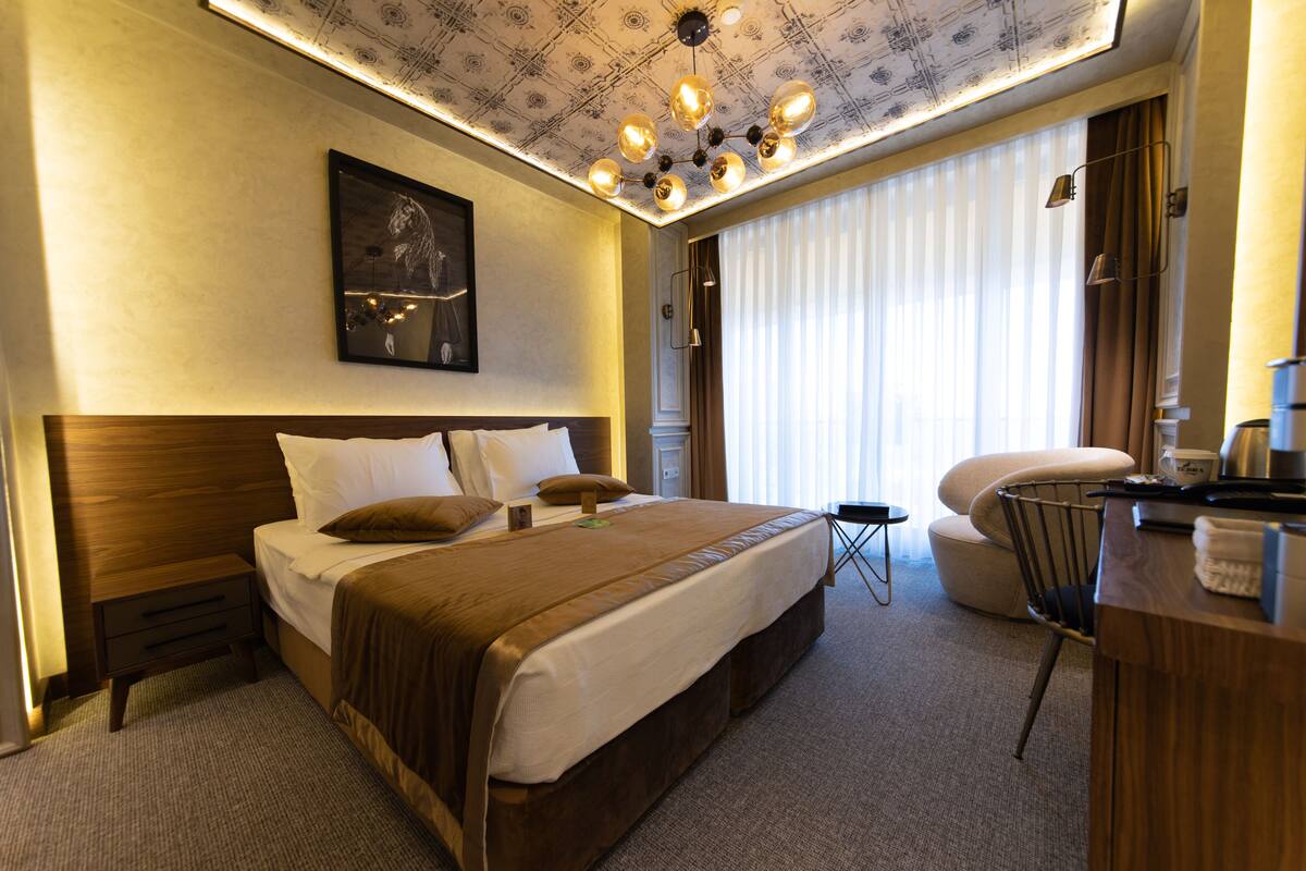 A hotel room with a large bed, a desk, a chair, and a ceiling light fixture.
