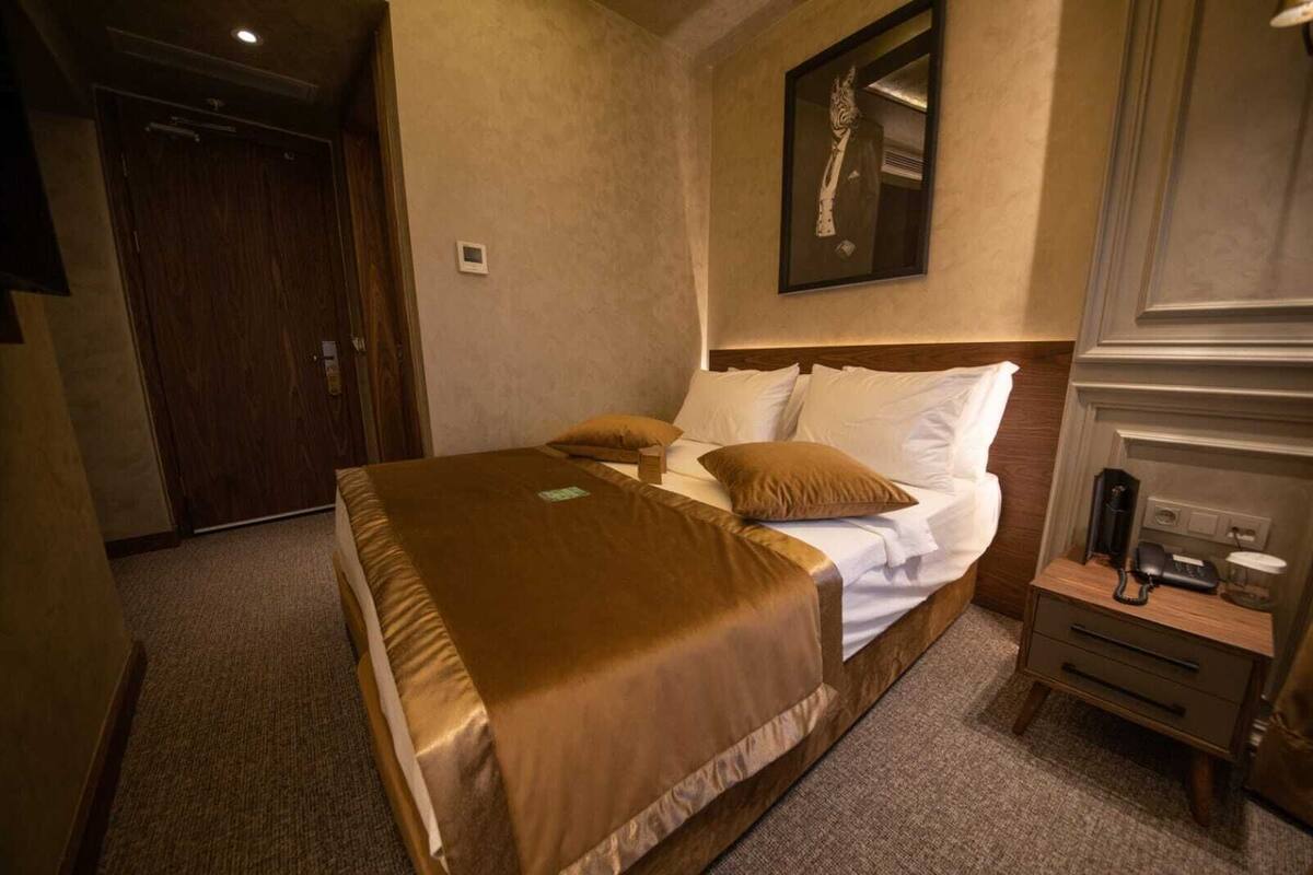A hotel room with a bed, a nightstand with a phone, and a mirror on the wall.