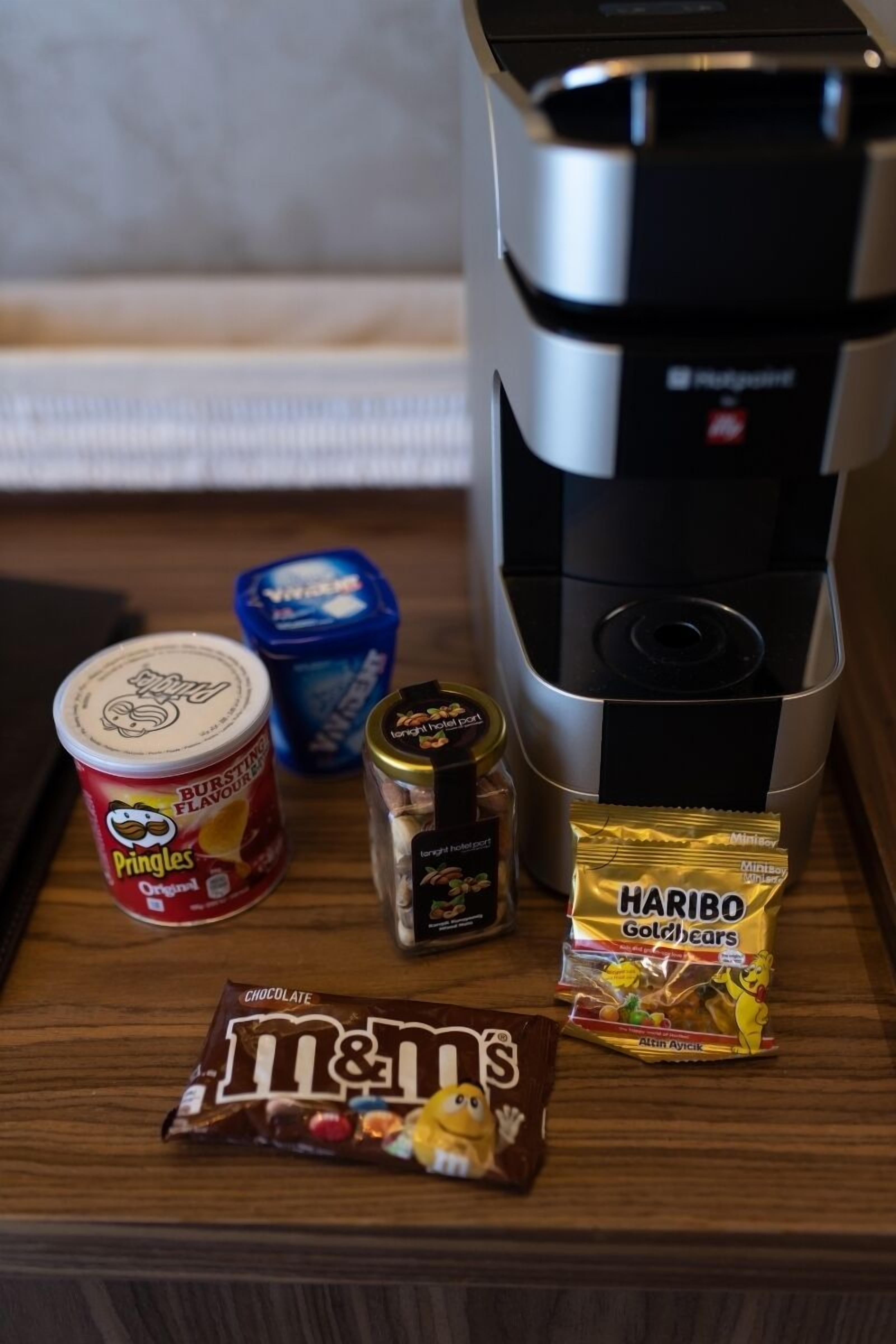 A coffee maker, a container of Pringles, a jar of coffee, a packet of Haribo Goldbears, and a chocolate bar on a wooden surface.