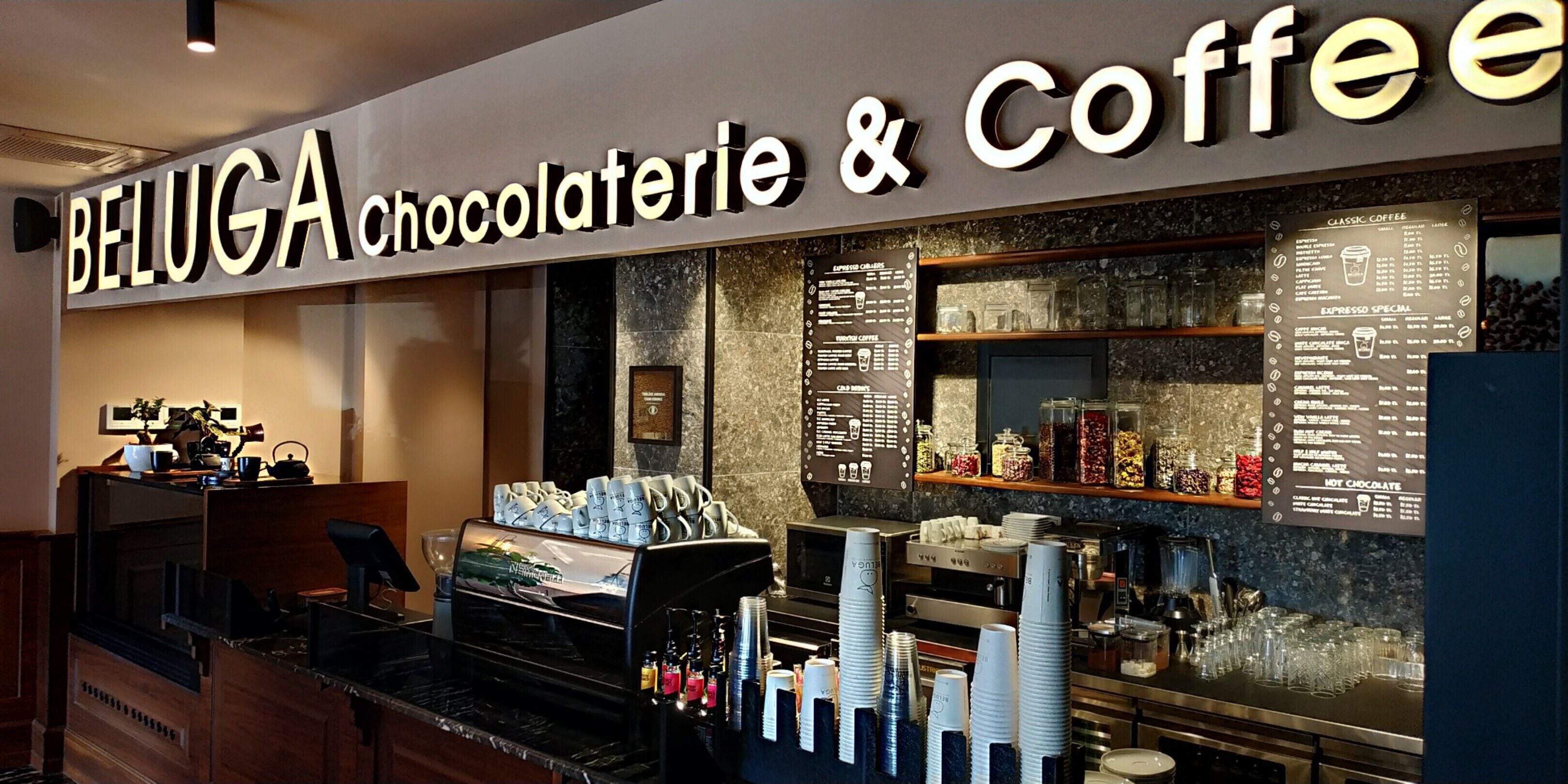 Un café-chocolaterie BELUGA, équipé d’une machine à café, de tasses et d’un tableau affichant le menu.