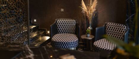 A modern interior with two patterned chairs, a small table with a vase of dried plants, and a decorative wall.