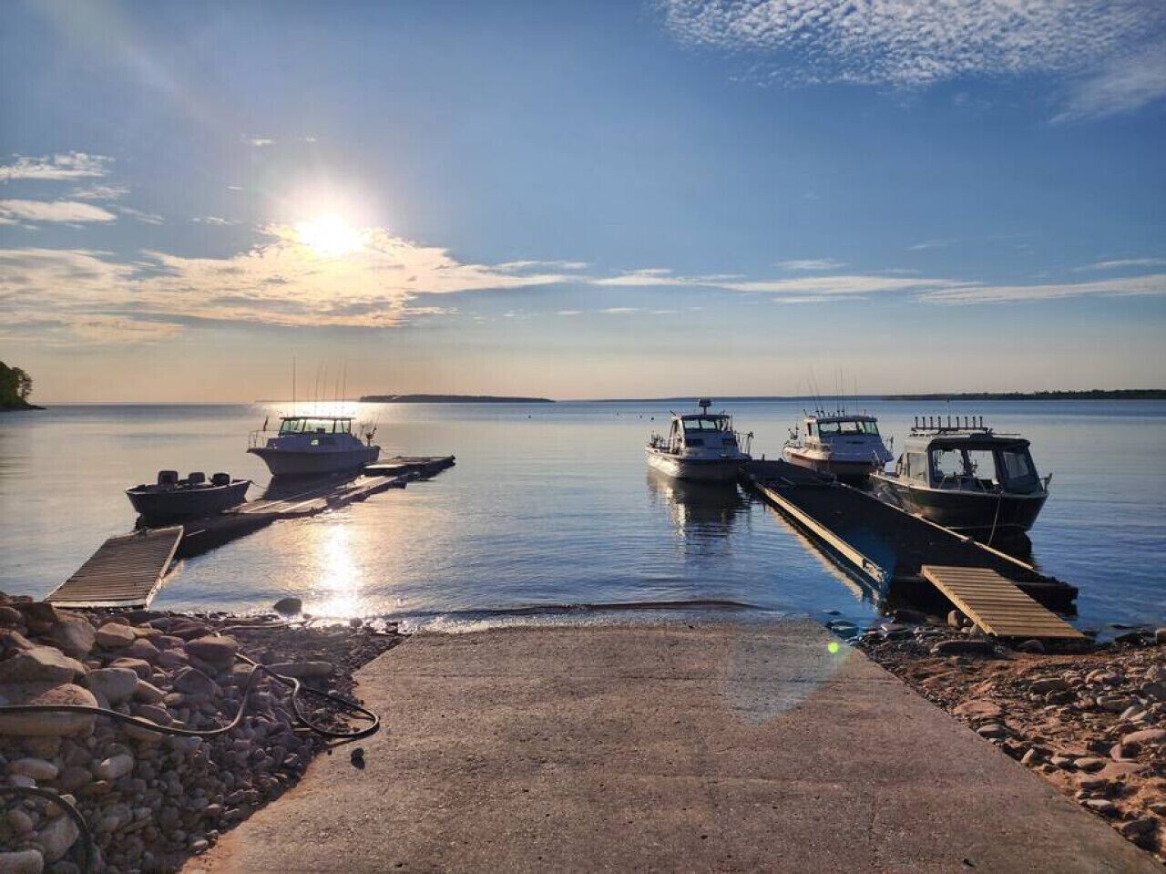 A calm lake with boats docked at a pier, surrounded by rocks and a clear sky.